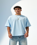 Man wearing a light blue oversized t-shirt and jeans against a light gray background