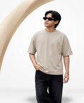 Person wearing a beige t-shirt and sunglasses standing against a white background