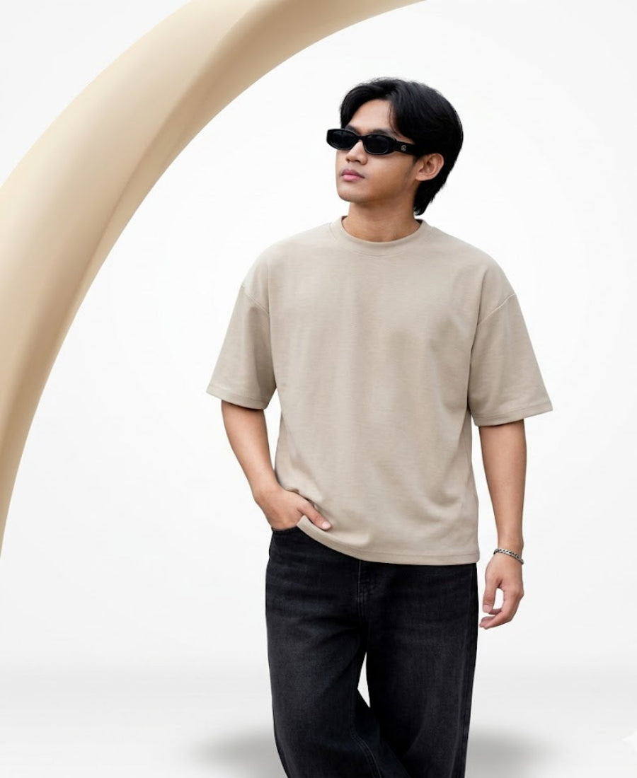Person wearing a beige t-shirt and sunglasses standing against a white background