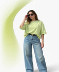 Woman wearing a light green oversized t-shirt and blue jeans against a white background