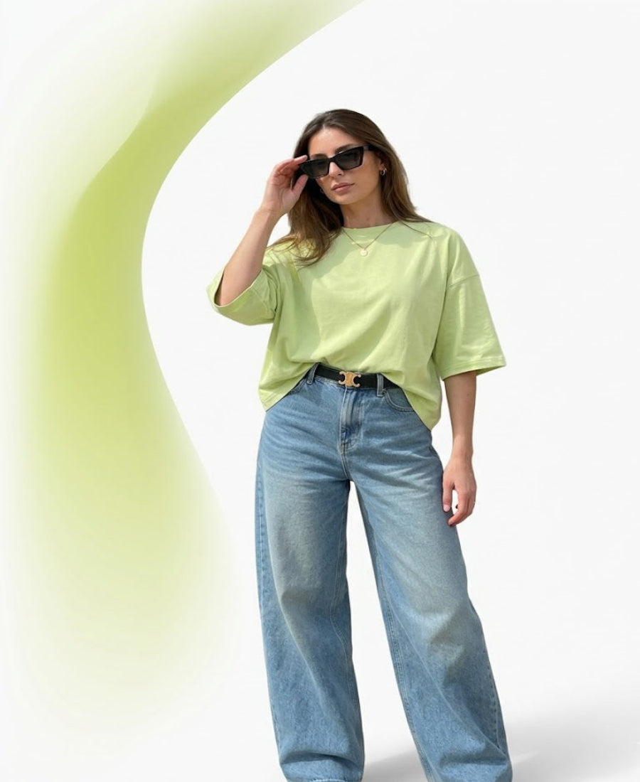 Woman wearing a light green oversized t-shirt and blue jeans against a white background