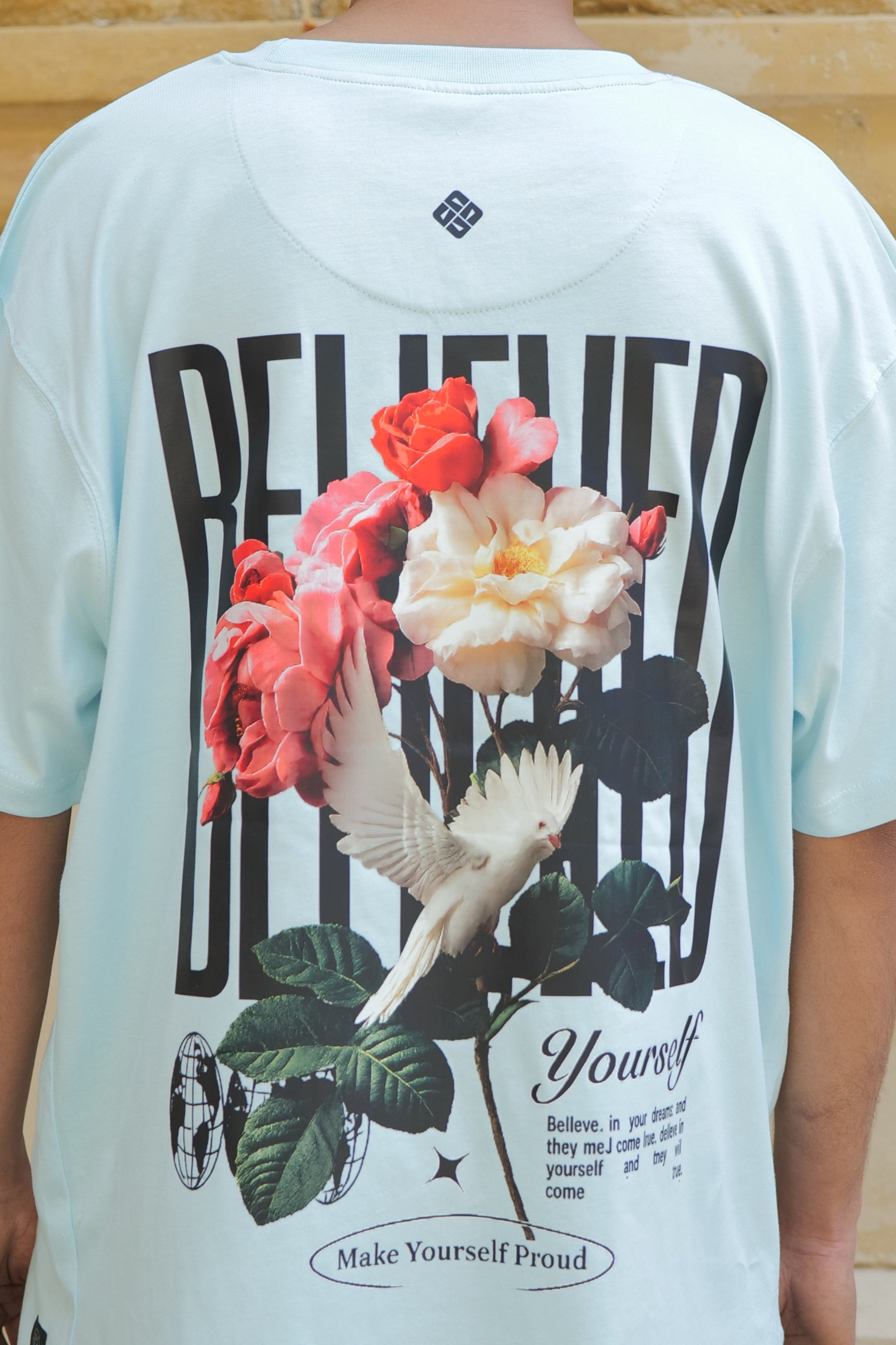 Person wearing a light blue t-shirt with floral design and text on a stone pavement background