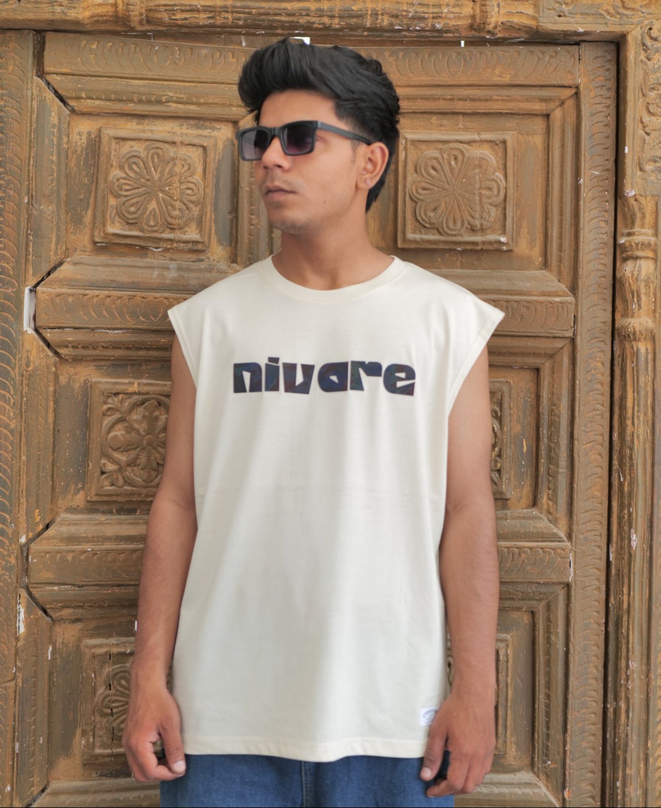 Person wearing a sleeveless shirt with 'nivare' logo in front of a wooden door.