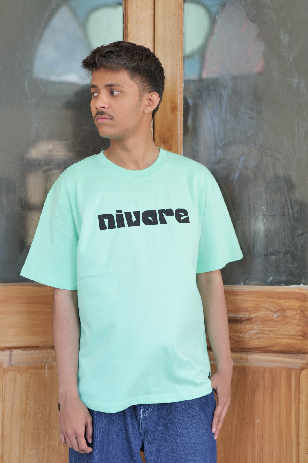 Person wearing a light blue t-shirt with 'nivare' logo in front of a wooden panel.
