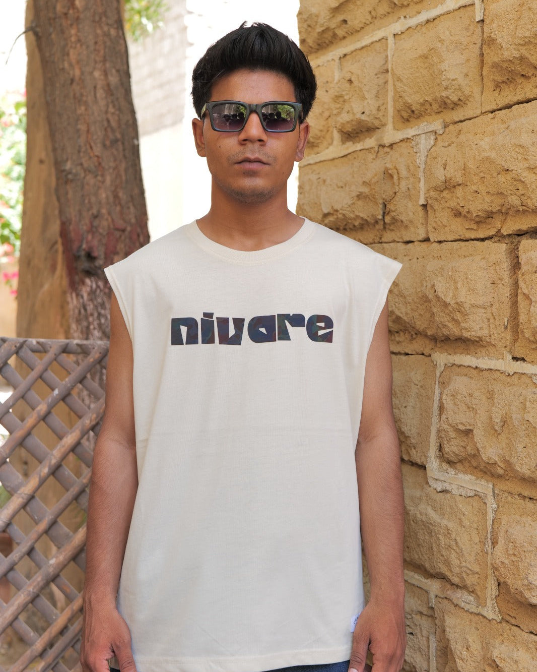 Man wearing a sleeveless shirt with 'nivare' logo standing against a stone wall.