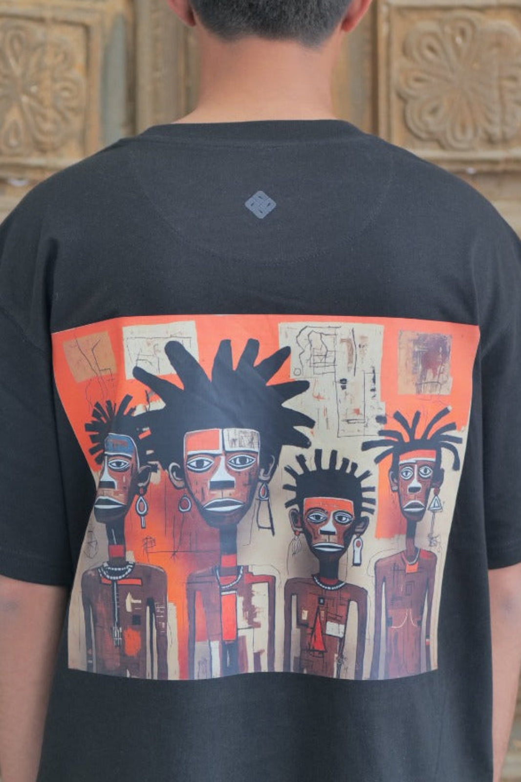 Person wearing a black t-shirt with a colorful graphic design in front of a wooden door.