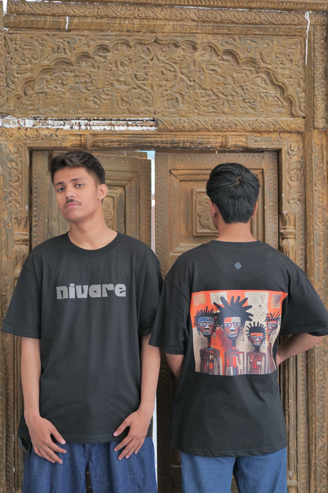 Person wearing a black t-shirt with 'nivare' branding on the front, standing in front of a wooden door.