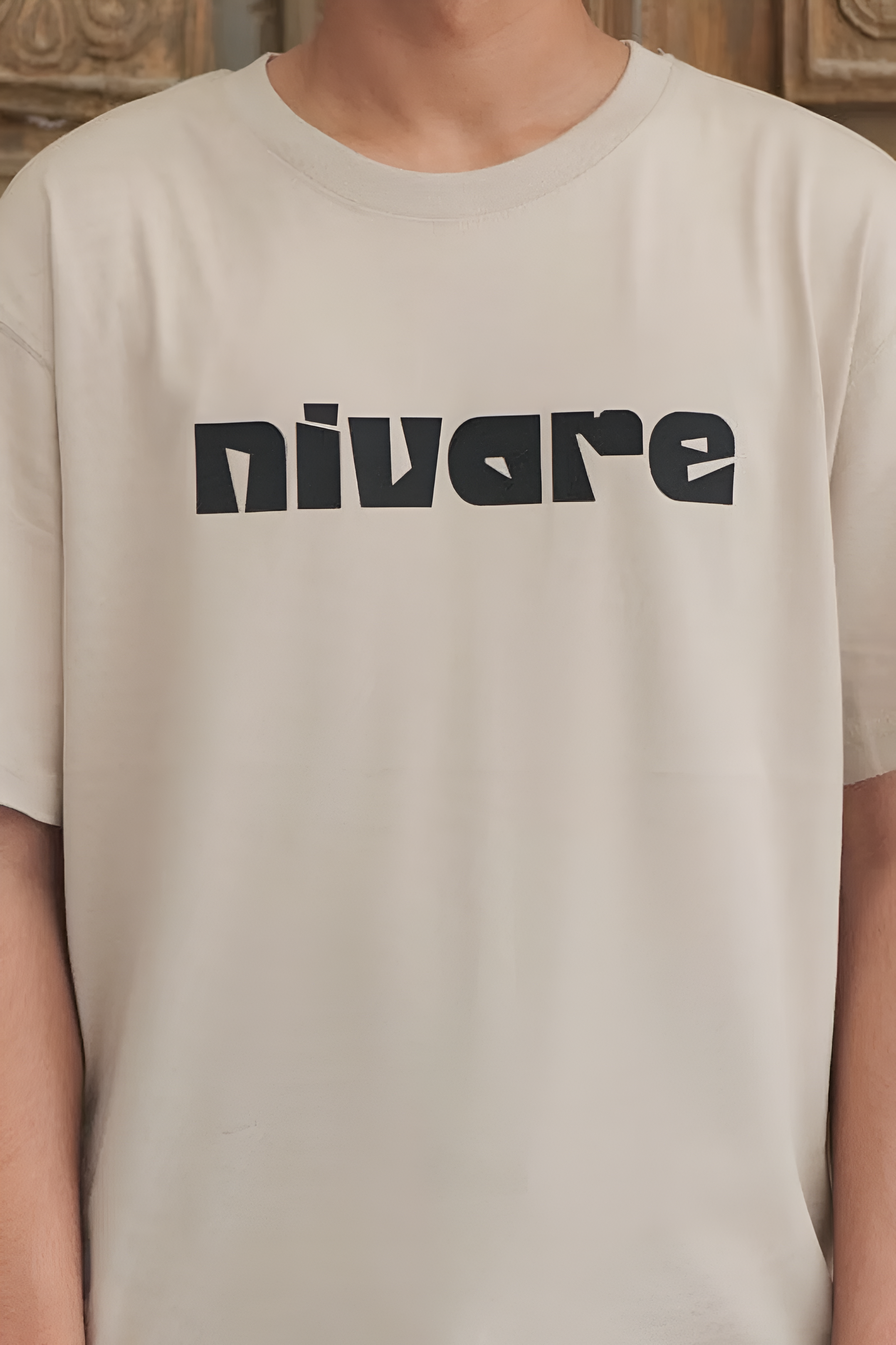 Beige t-shirt with 'nivare' printed on it worn by a person.