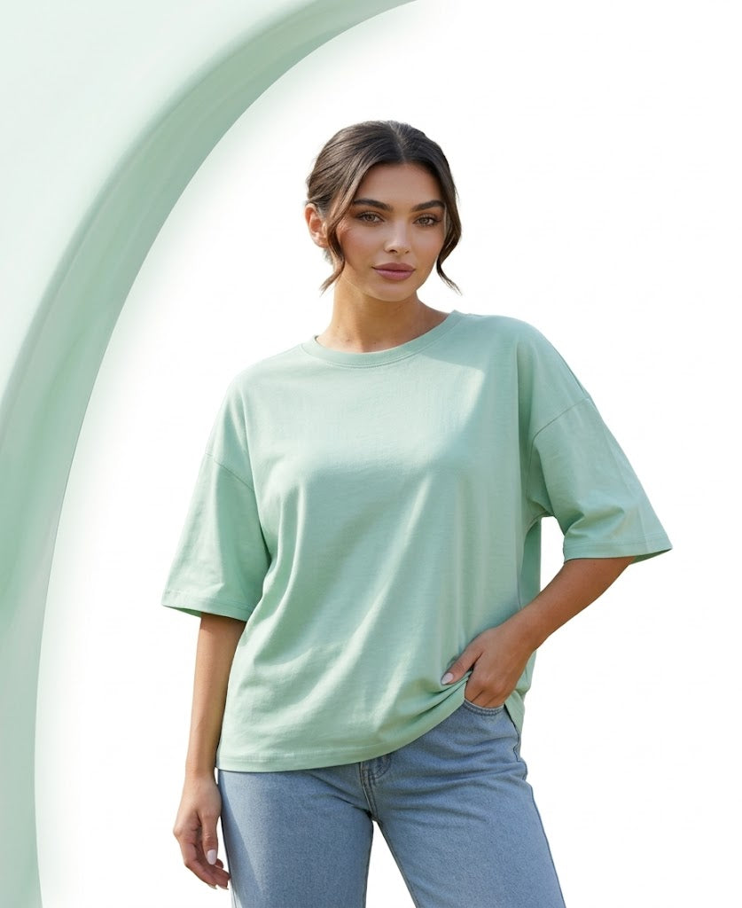 Woman wearing a light green oversized shirt and blue jeans against a light green background