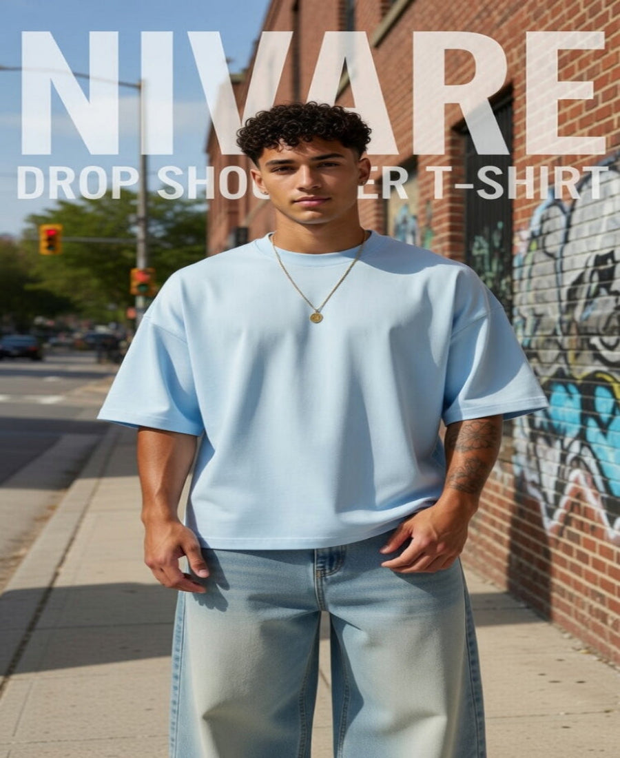 Man wearing a light blue t-shirt and jeans standing on a sidewalk with graffiti in the background, promoting Nivare t-shirts.
