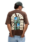 Person wearing a brown t-shirt with a floral design and text on the back, standing against a plain background.