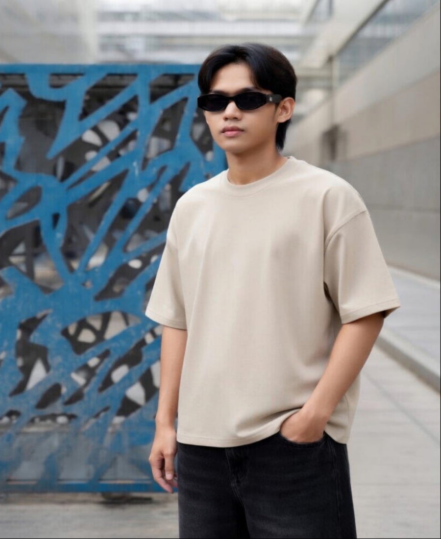 Person wearing a beige t-shirt and sunglasses standing in front of a blue textured wall.