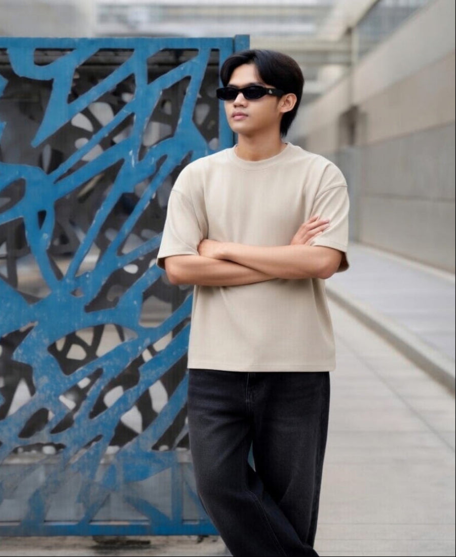 Man wearing sunglasses and a beige shirt standing in front of a blue metal gate.