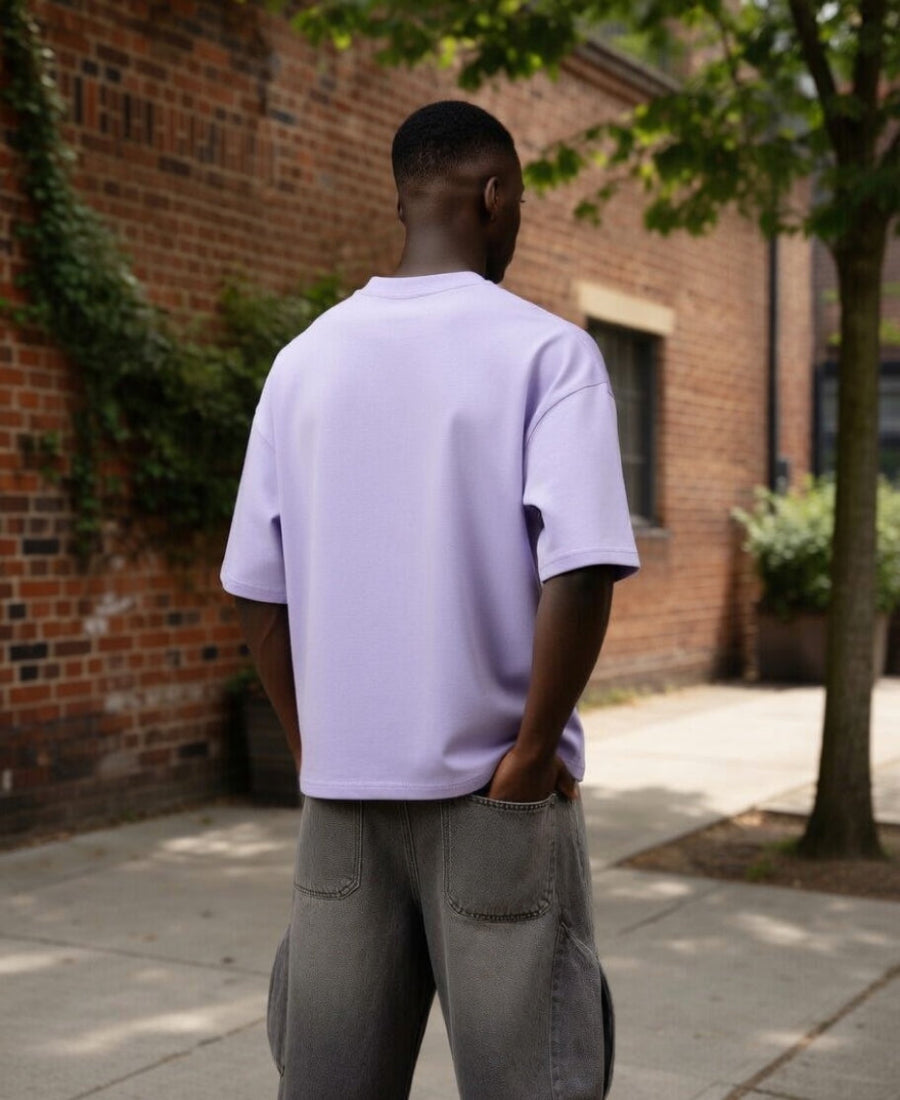 Person wearing a light purple t-shirt and gray cargo shorts standing in front of a brick wall.